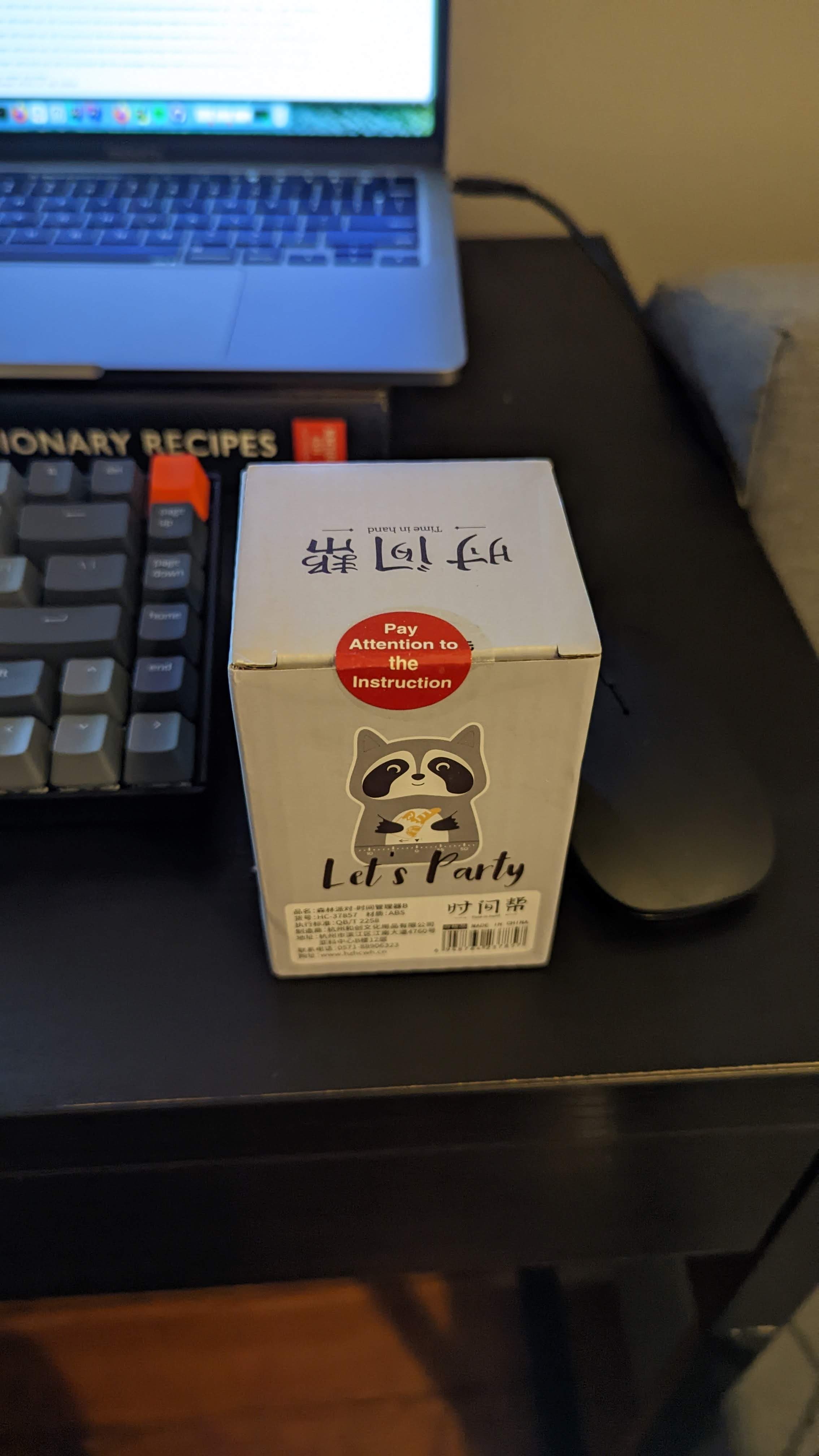 A box containing a racoon timer with a sticker over the opening that reads "Pay Attention to the Instruction"